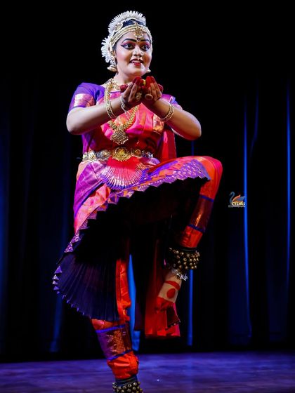 A powerful pose from a classical Indian dancer, captured with dramatic lighting that emphasizes her form and traditional attire.