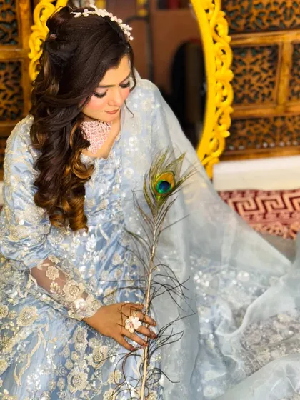 A closer look at the soft makeup, featuring a pink-toned necklace and a delicate hair accessory. The peacock feather adds a touch of traditional artistry.