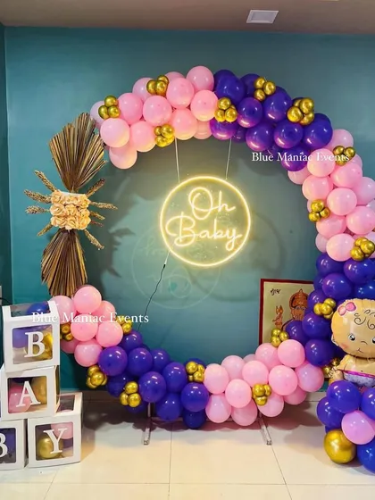 Celebrating a new arrival is always special. This 'Oh Baby' shower decoration uses a full balloon ring in shades of pink and purple, accented with gold chrome balloons, a custom neon sign, and 'BABY' display boxes for a joyful and picture-perfect event.