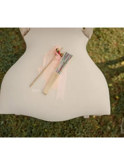 A simple, elegant detail for guests at a garden wedding. A hand fan and a bell wand are placed on each chair, providing comfort for the sunny ceremony and a way for guests to joyfully cheer for the couple.