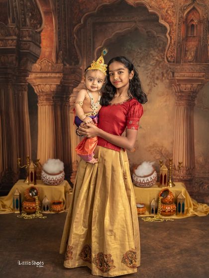 An older sister proudly holds her baby sibling, who is dressed as Krishna. This is a wonderful way to include the whole family in the festive celebration.