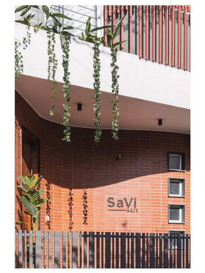 The entrance detail of the 'SaVi' residence, also known as the 'House Under Tabebuia Trees'. The name is elegantly integrated into the brickwork beneath a dramatic cantilevered roof with hanging plants.