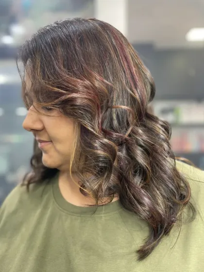 A side view of a curly, layered haircut with subtle red and blonde highlights, creating a multi-dimensional and textured look.
