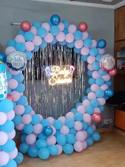 A classic pink and blue baby shower ring with a silver shimmer backdrop and baby bottle foil balloons.