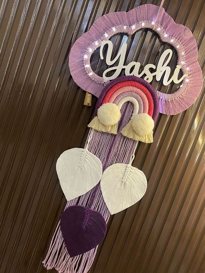 This angled shot of the 'Yashi' nameplate highlights the texture of the macrame leaves and the neat wrapping of the rainbow and cloud.