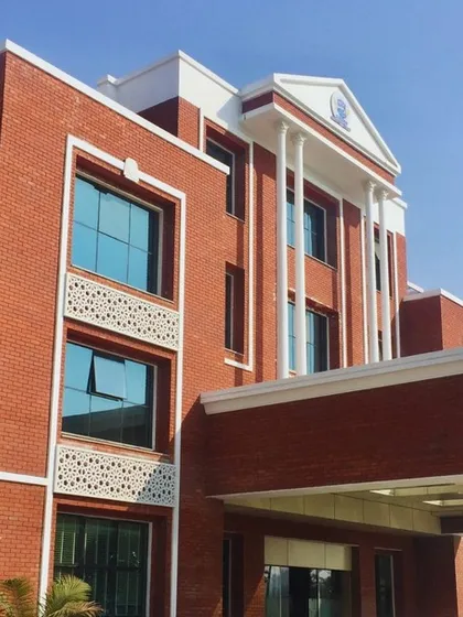 An angled view of Prayag International School, highlighting the classical architectural elements like pediments and pillars combined with a modern red brick and glass material palette.