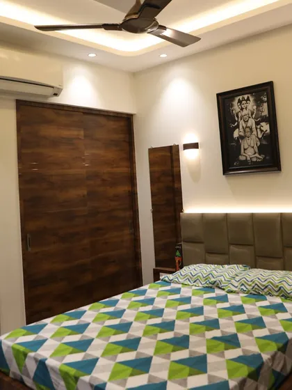 A bedroom with a dark wood sliding wardrobe and a custom padded headboard. The wall-mounted lights and the personal photo frame make the space feel cozy and personalized.