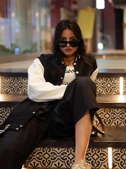 A relaxed portrait of a model sitting on illuminated stairs. The modern setting and her casual outfit create a cool and contemporary street style look.