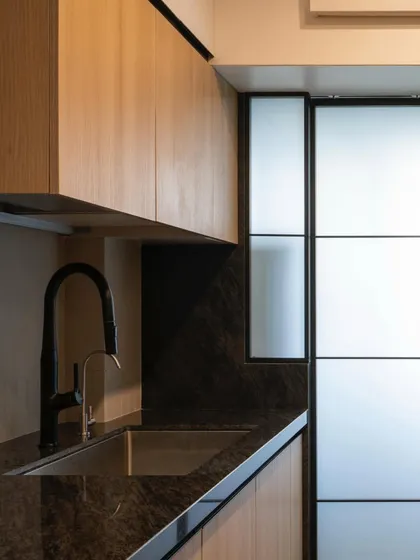 A compact parallel kitchen where warm wood tones and a dark countertop create a sleek, modern aesthetic. The frosted glass sliding doors conceal a utility area, keeping the main space uncluttered.