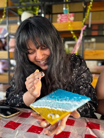A participant smiling with her finished beach texture art. The joy of creating something beautiful with your own hands is what our workshops are all about.
