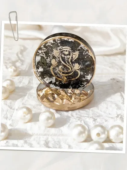 Bless your space with a divine touch. This customized mini Ganesh Ji stand features a black and gold design, surrounded by pearls. It's perfect for a car dashboard, office desk, or as a thoughtful gift.