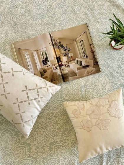 Our hand-detailed cushions and jacquard rug create a moment of soft luxury. The image shows our embroidered and patterned cushions alongside a design magazine, reflecting our passion for beautiful interiors.