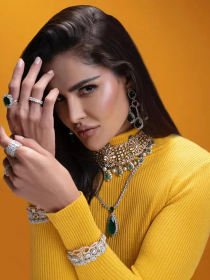 A full-body shot of the emerald and diamond jewellery set against a vibrant yellow turtleneck. This styling choice was made to create a modern, high-fashion look that is both chic and daring.