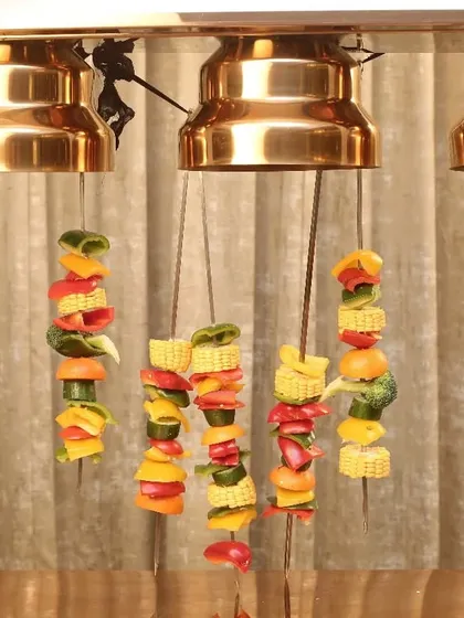 A unique way to serve and keep food warm. These colorful vegetable skewers are hung from a heated lamp stand, creating a visually interesting display and ensuring they are served at the perfect temperature.