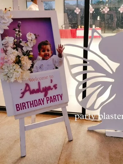 We create personalized welcome easels for our events. This one for Aadya's party features a photo of the birthday girl, custom text, and is decorated with a fairy cutout and flowers.