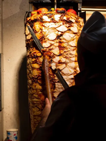 A master at work carving a massive döner kebab spit. This image is powerful, showing the scale and tradition of this iconic dish.