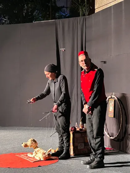 A dog marionette from 'Pay Attention to Those Two' is prepared for its scene. The level of detail in the puppet, combined with the puppeteer's focus, promises a captivating performance.