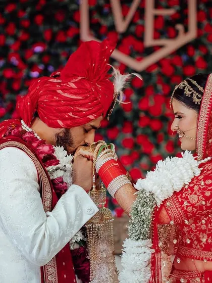 A gesture of love and respect. The groom gently kisses the bride's hand after the ceremony, a tender moment against a backdrop of red roses.