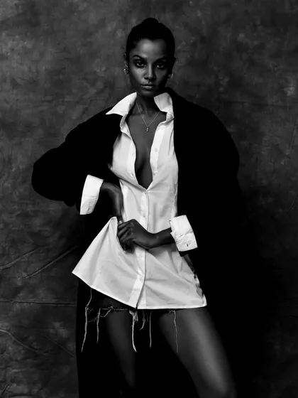A high-fashion black and white shot with dramatic styling. The contrast between the white shirt and black coat creates a bold, graphic look.