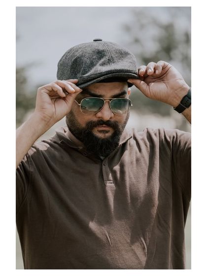 A casual outdoor portrait of a man with a beard and cap. The natural setting and relaxed pose create an authentic and approachable feel.