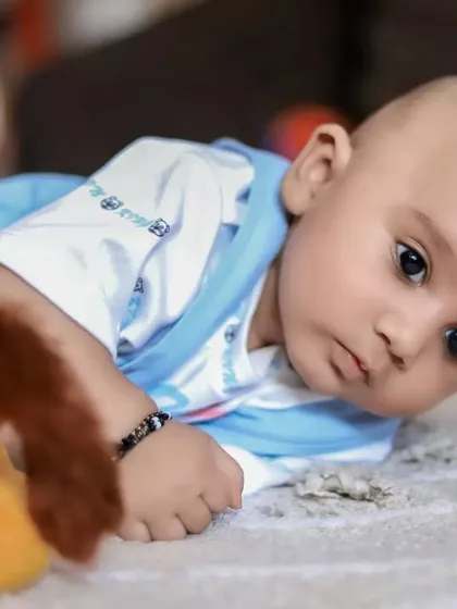 A tender profile of a baby lying on a soft rug next to a toy. This shot captures their delicate features and calm demeanor.