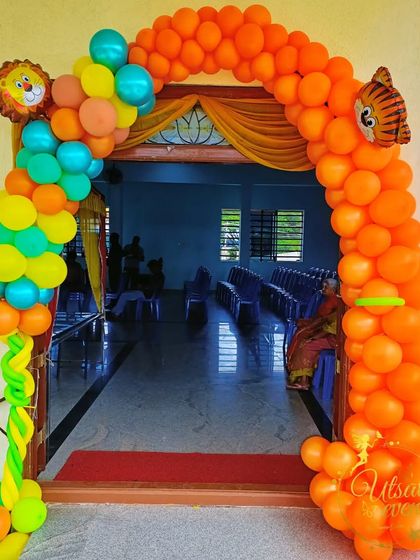A colorful jungle-themed balloon arch at the entrance of a party hall. The arch is decorated with lion and tiger balloon figures, welcoming guests to the celebration.