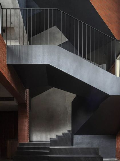 The main stairwell of the Brick House, where the black geometric staircase connects the different levels, weaving through spaces defined by exposed brick and concrete.