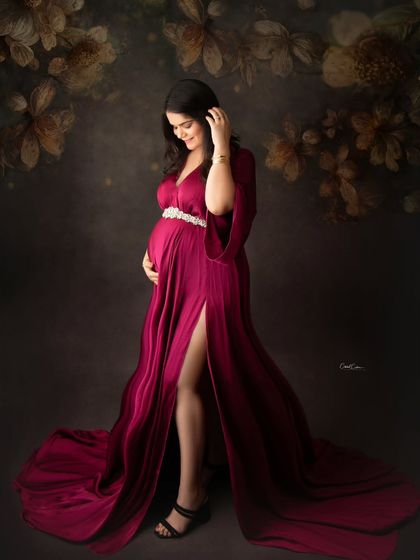A beautiful portrait against a floral backdrop. The mom-to-be looks stunning in a deep magenta satin gown with a thigh-high slit.