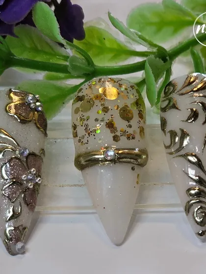 An example of classic elegance, these nails feature intricate gold chrome scrollwork over a pearly white base. The designs include floral motifs and a 3D ring accent, perfect for a bridal or formal occasion.