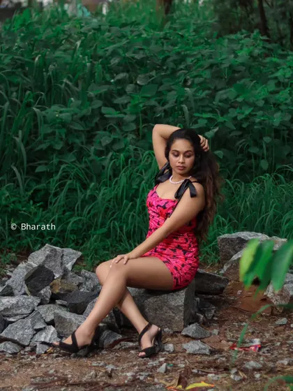 A full-body shot of the model in the pink dress, seated on rocks in a forest-like setting.