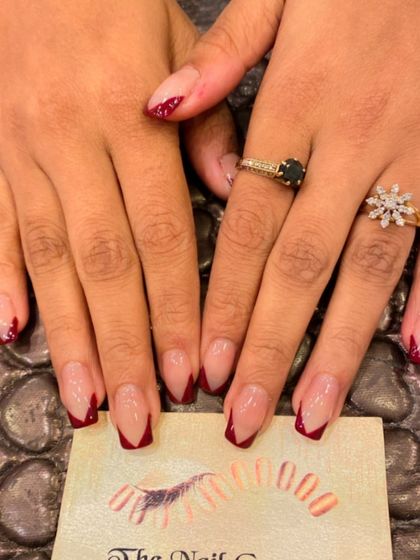 A dramatic V-shaped French manicure on coffin-shaped nails. The sheer nude base is paired with deep red tips for a bold and sophisticated look.