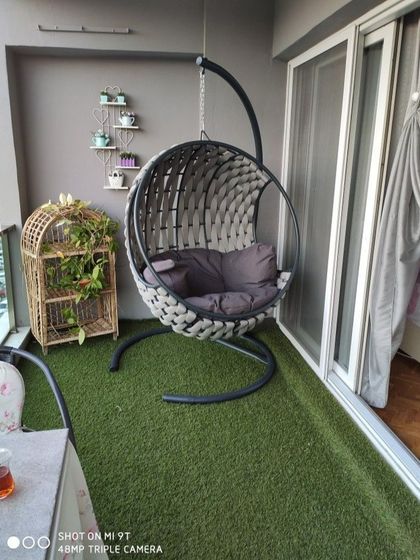 This simple yet effective balcony setup uses artificial grass to instantly add a touch of green. A comfortable swing chair and a small decorative shelf complete this cozy and low-maintenance space.