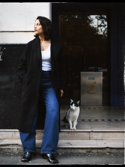 A full-length portrait of a woman and a cat, standing on the steps of a building. It feels like a scene from a classic European film.