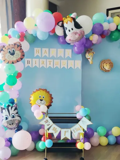A colorful and cute animal-themed decoration for a first birthday. This home setup features a pastel balloon arch, a 'Happy Birthday' banner, and various animal foil balloons.