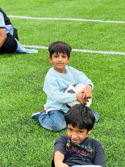 Two boys take a break on the football field, sharing a moment of friendship. My sports programs are designed not just to teach skills but also to foster social connections and sportsmanship.