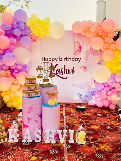 A lovely outdoor butterfly-themed party for Kashvi. The setup is arranged on a terrace, featuring a pastel balloon arch and themed pedestals.