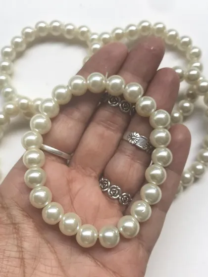 Holding a classic pearl bracelet. The smooth, uniform pearls make for a comfortable and versatile piece of jewellery that complements any style.