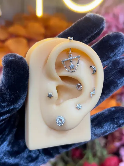 A celestial-themed ear stack on a model, featuring a star and chain hanging, moon stud, and other sparkling pieces.