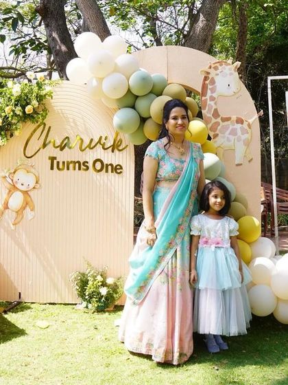 The birthday boy Charvik's mom and sister posing by a custom "Charvik Turns One" photo board and a cute train prop.