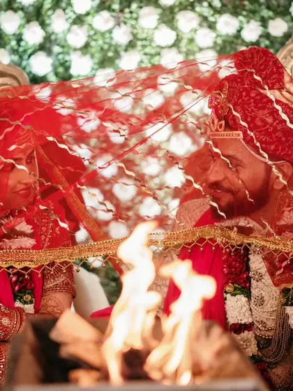 A sacred moment by the holy fire. The couple, veiled together, share a private glance, symbolizing their union in the presence of Agni, the divine witness.