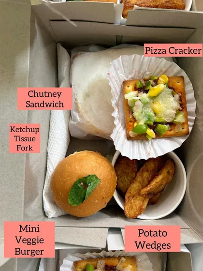 A closer look at one of my custom snack boxes. This one contains a Mini Veggie Burger, a classic Chutney Sandwich, crispy Potato Wedges, and a cheesy Pizza Cracker, along with ketchup and a napkin.