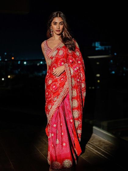 A model glows in a red and pink bandhani saree with heavy embroidery, perfect for an evening celebration.