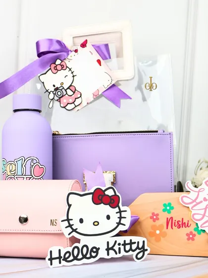 All the items from our "Hello Kitty" hamper displayed. This set includes a "Self Love" water bottle, a purple utility pouch, a pink cardholder, and a custom wooden nameplate.
