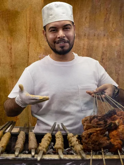 Our chef proudly presenting skewers of freshly grilled kebabs. We serve our food with a smile because we are proud of the quality we deliver.