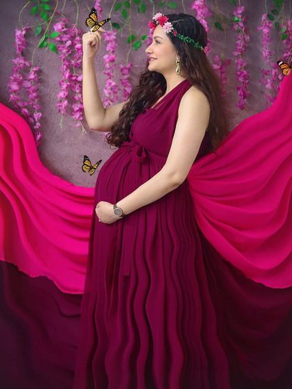 Feeling like a goddess in this whimsical studio setup. The flowing magenta gown, flower crown, and magical butterflies create a truly enchanting maternity portrait.