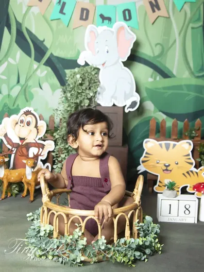 A 'Wild One' jungle adventure for a first birthday. This photo shows the complete themed setup with friendly animal cutouts, lush greenery, and a rustic basket for the perfect explorer portrait.