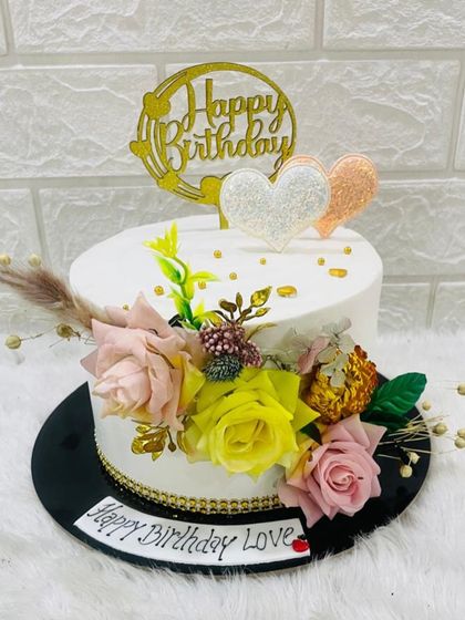 A lovely birthday cake decorated with a beautiful bouquet of pink, yellow, and white sugar flowers and delicate dried botanicals.