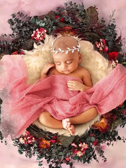 A newborn wrapped in a pink cloth, resting in a nest decorated with red and green foliage.