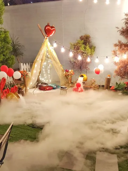 A whimsical teepee setup enveloped in a thick layer of low-lying fog. This dramatic effect, combined with string lights and balloons, creates a mysterious and magical ambiance for a surprise celebration.