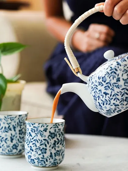 A dynamic shot of tea being poured from a ceramic teapot, adding a sense of action and warmth to the image.